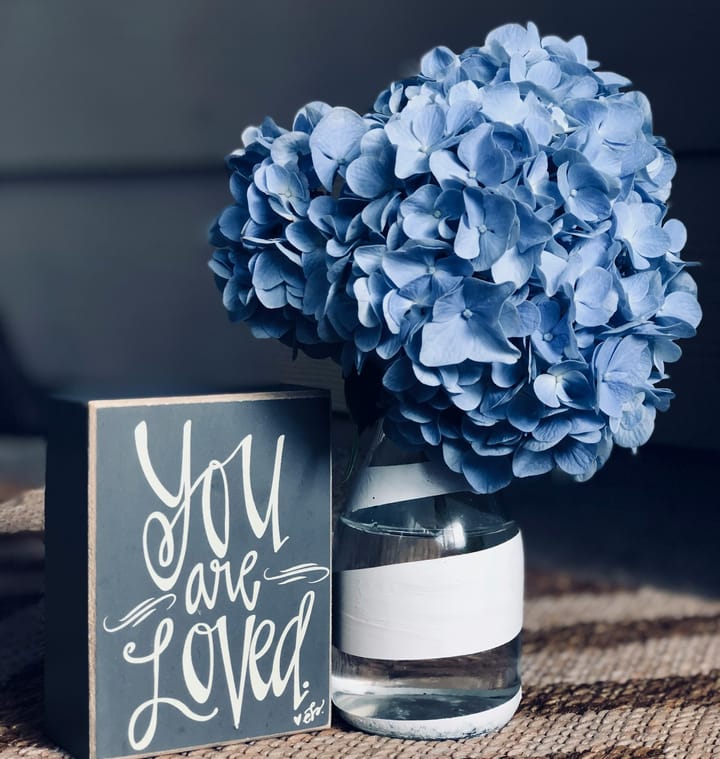 "You are Loved" sign and blue flowers in a glass vase